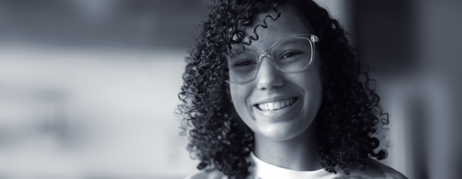 Photo of a teenage biracial girl with glasses and curly hair, smiling at the camera