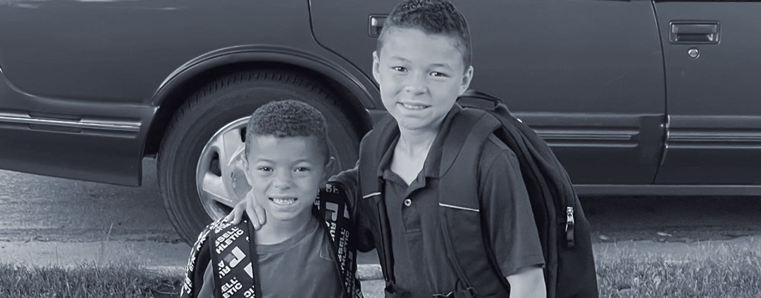 two young boys standing in front of a car