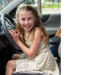Rosalee, an eight year old girl, sitting in the front seat of a car pretending to drive