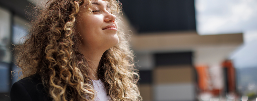 A young woman with curly hair looking upward and breathing in deep