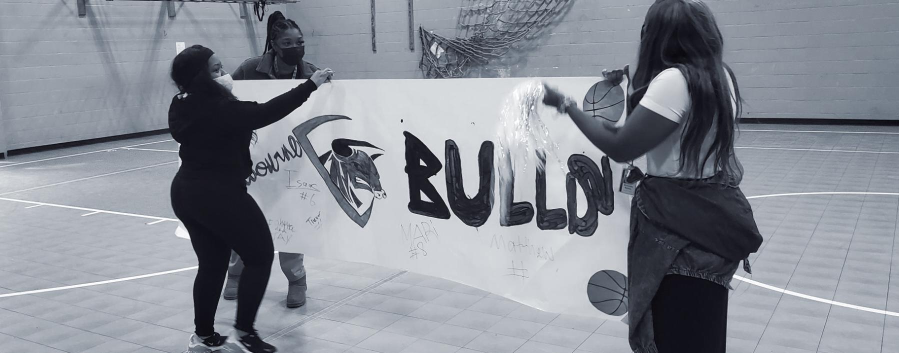Nexus-Woodbourne staff holding up a handmade sign to celebrate another win for their basketball team, the Midnight Bulls