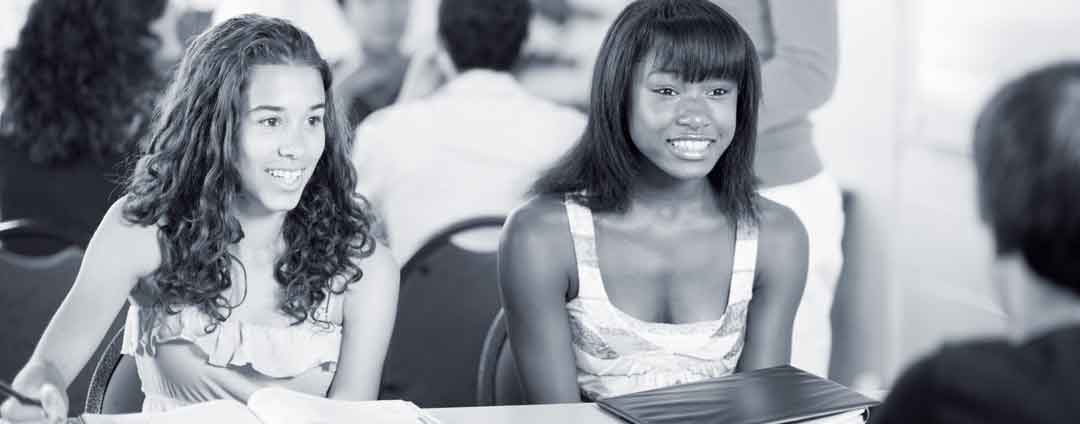 Two teenage girls sitting at a table talking to an adult