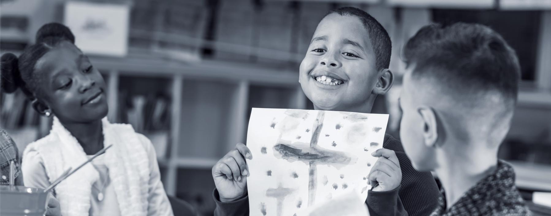 Photo of a young boy showing off his artwork to classmates