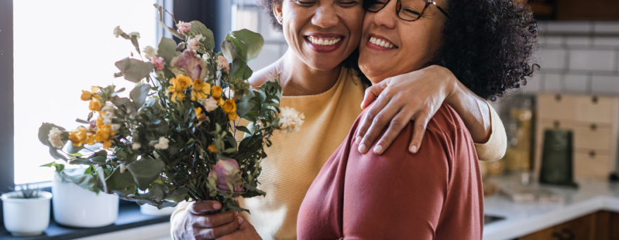 Two women smiling and embracing with the exchange of a bouquet of flowers