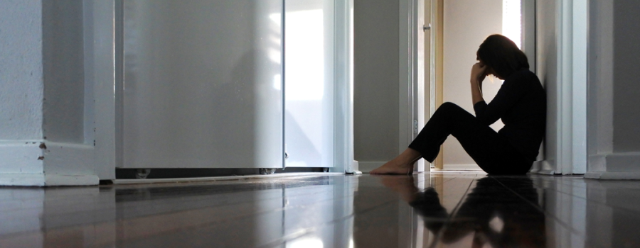 Picture of a woman sitting alone on the floor with her head down.