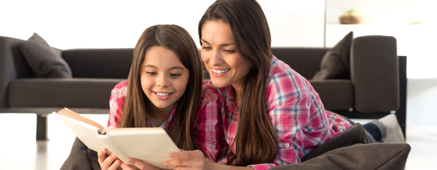 A woman and a child sitting together reading and smiling.