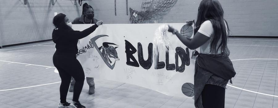 Nexus-Woodbourne staff holding up a handmade sign to celebrate another win for their basketball team, the Midnight Bulls