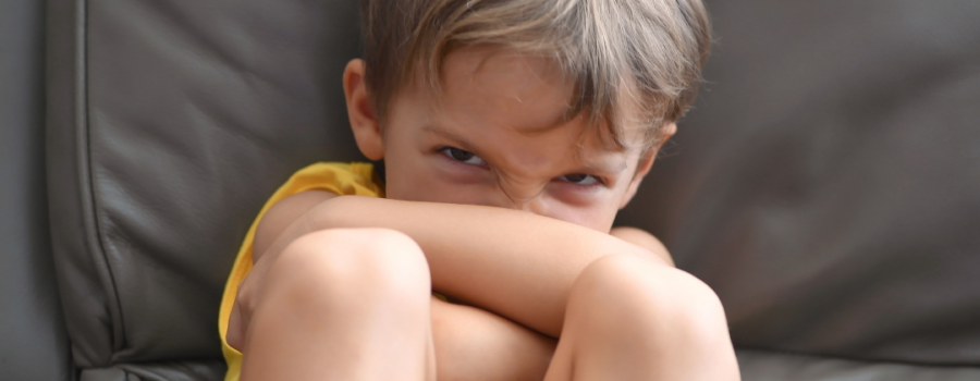 Photo of a young blond haired boy sitting on a couch angry