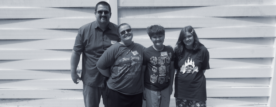 Kayleigh's family photo - a photo featuring dad, mom and brother alongside Kayleigh standing in front of a white fence. 