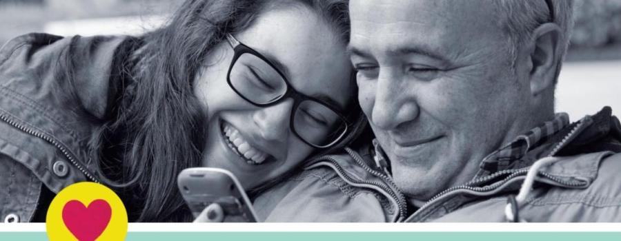 A man and a woman sitting side by side both smiling at a phone.