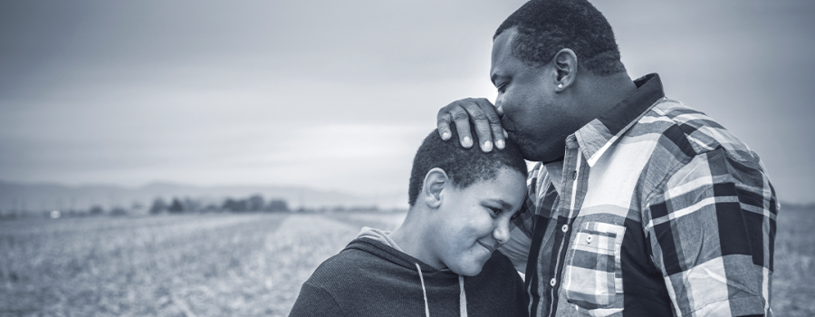 Black father kissing the forehead of his son while overlooking a grassy field