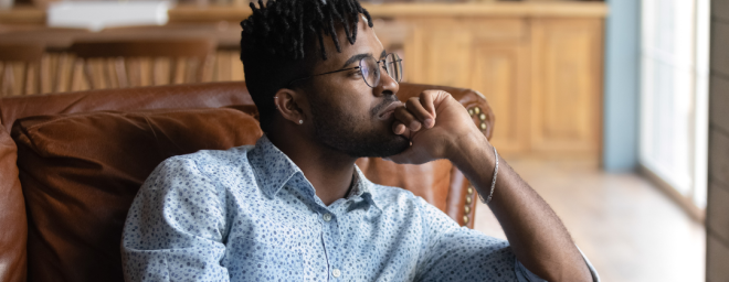 A Black man sitting in a chair with his head on his hand in a pensive, thoughtful pose