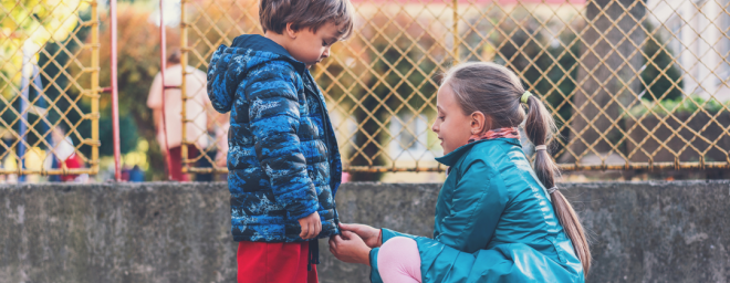 A young girl zipping up a coat of a younger boy