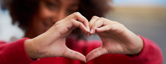 A Black woman create a heart shape with her hands