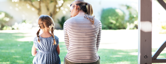 Mother with a young daughter sitting outside, with their backs to the camera.