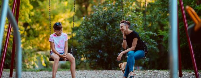 Picture of a parent and a child sitting on swings, having a conversation.