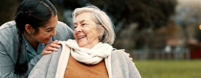 A younger woman holding the shoulders of an elderly woman and smiling