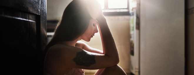 Young woman sitting on the floor with her head in her hands as the sunlight hits her face