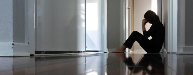 Picture of a woman sitting alone on the floor with her head down.
