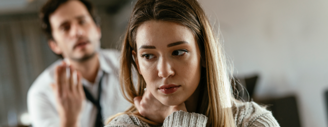 Picture of a wife seeming anxious, while her husband is in the background pleading to her.