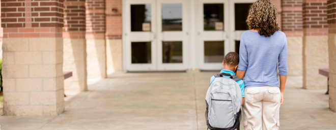 A mother holding her son's hand as they stand in front of a school