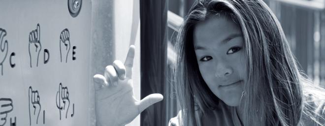 An Asian teenage girl signing the letter L in American Sign Language
