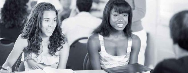 Two teenage girls sitting at a table talking to an adult