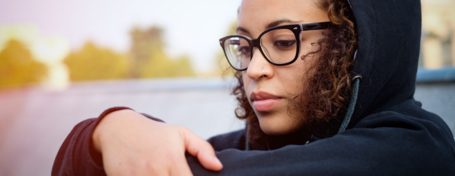 teenage girl sitting crouched holding her knees with a sad look on her face