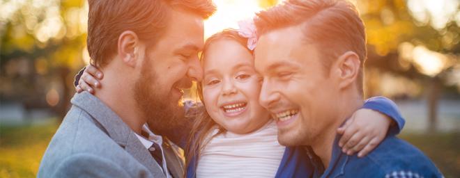 Two dads hugging and holding a young girl