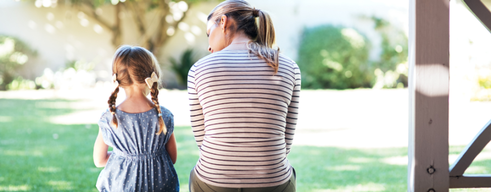 Mother with a young daughter sitting outside, with their backs to the camera.