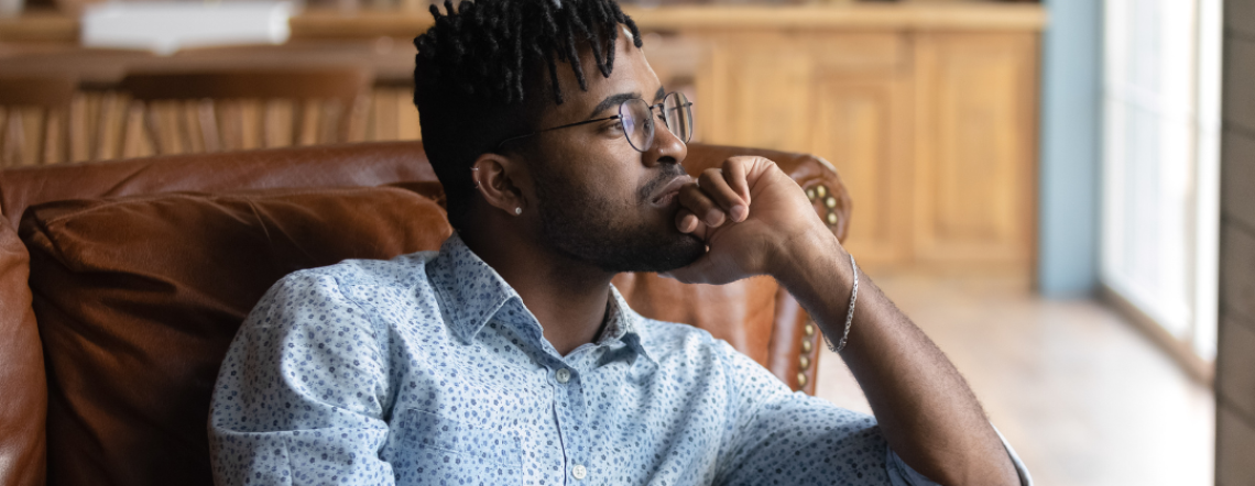 A Black man sitting in a chair with his head on his hand in a pensive, thoughtful pose