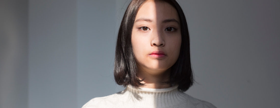 Picture of an Asian woman caught in the shadow. Half of her body in standing in the light, half in the shadow.