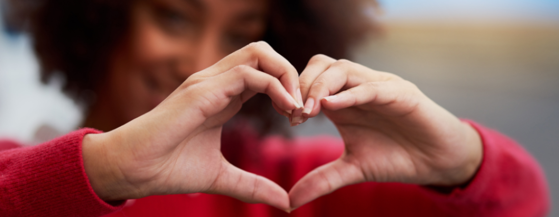 A Black woman create a heart shape with her hands