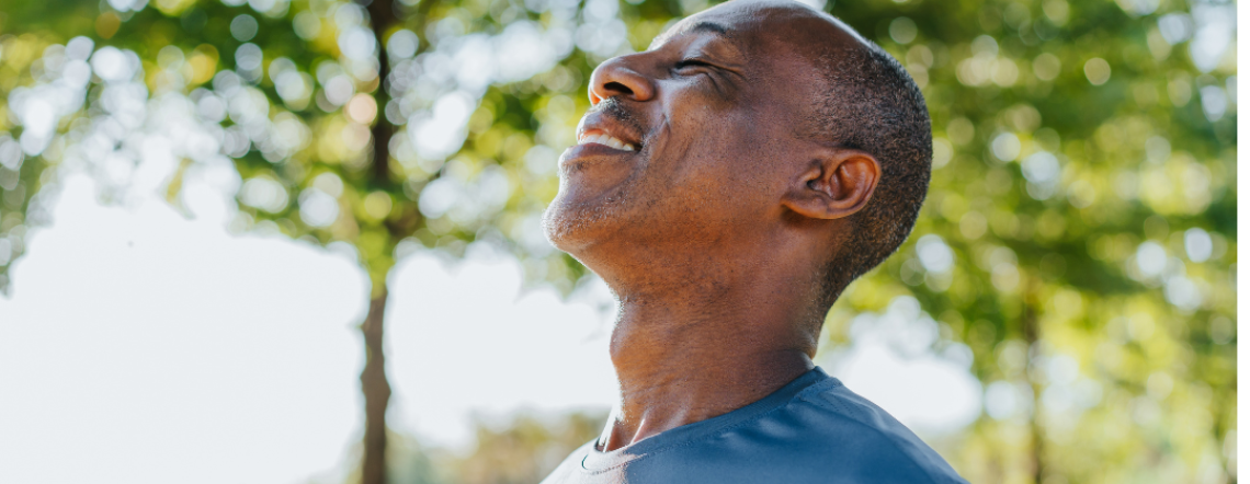 An adult Black male deeply breathing in fresh air while outside under a tree