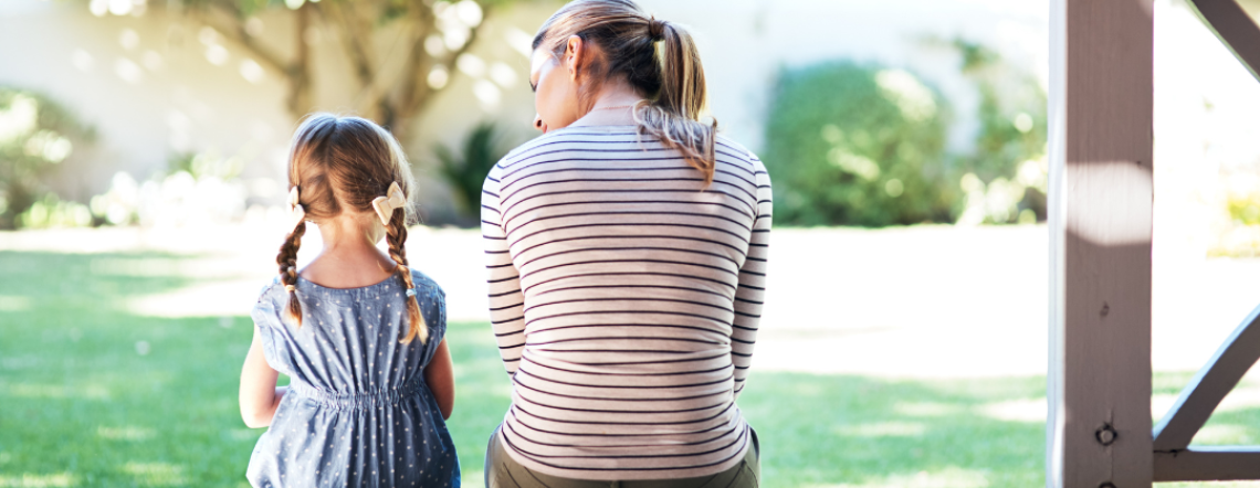 Mother with a young daughter sitting outside, with their backs to the camera.