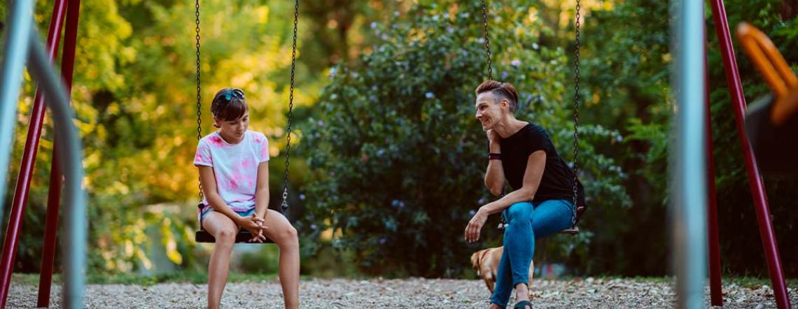 Picture of a parent and a child sitting on swings, having a conversation.