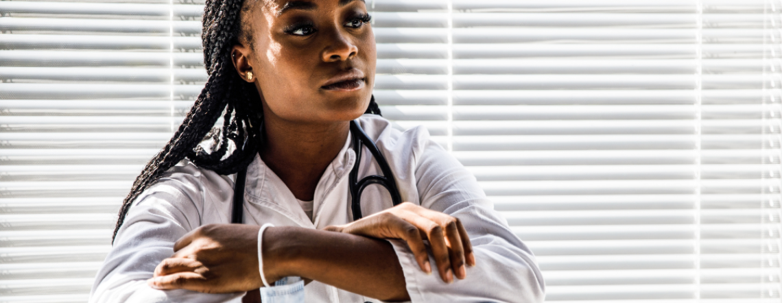 A young black woman sitting near an office window looking pensive