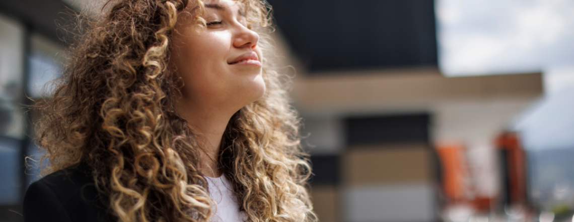A young woman with curly hair looking upward and breathing in deep