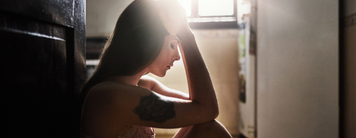 Young woman sitting on the floor with her head in her hands as the sunlight hits her face