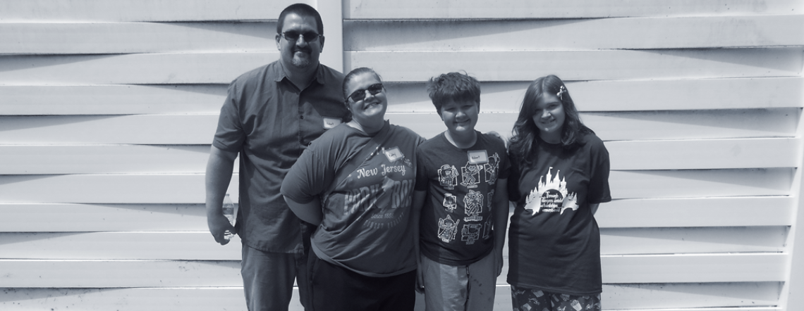 Kayleigh's family photo - a photo featuring dad, mom and brother alongside Kayleigh standing in front of a white fence.