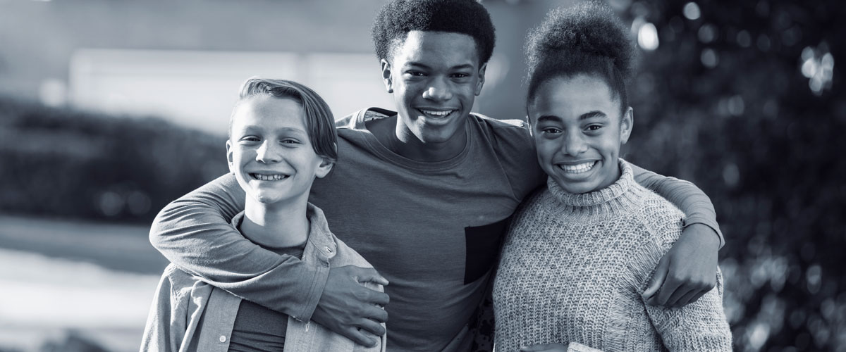 Three multi-racial youth smiling with arms around each other